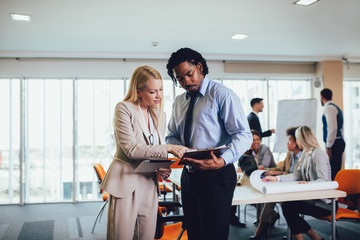 Portrait of two young businesspeople using digital tablet while colleague in background. Selective focus
