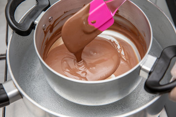 Cooking pot with chocolate melting being removed by chef´s hand on the stove of a kitchen to make sweet desserts. Bulk chocolate melting in a pot.