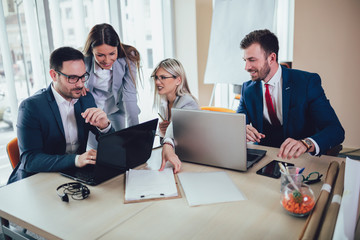 Group of young business people working and using laptop while sitting at the office desk together. Selective focus.
