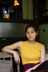 Fototapeta na wymiar Asian chinese girl having a good time at a coffee shop in hangzhou, China. wearing a yellow tank top and a reddish patterned dress with pants. holding a hand bag