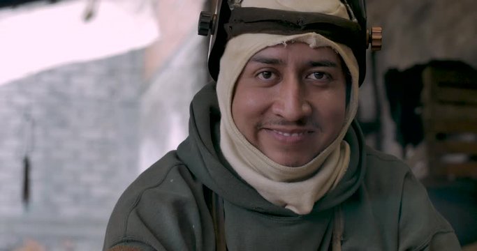 Latino man lifting up a welding mask, smiling, and looking at camera