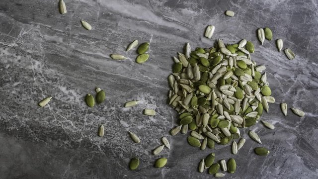 Pumpkin And Sunflower Seeds scattered on a marble stone background overhead shot with a pan, zoom and rack focus effect.