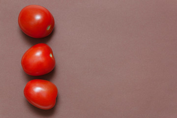 Three red fresh tomatoes lie on a brown background
