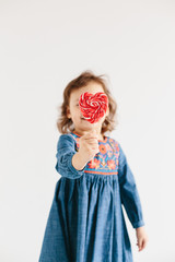 Little girl eating red heart shape lollipops