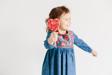 Little girl eating red heart shape lollipops