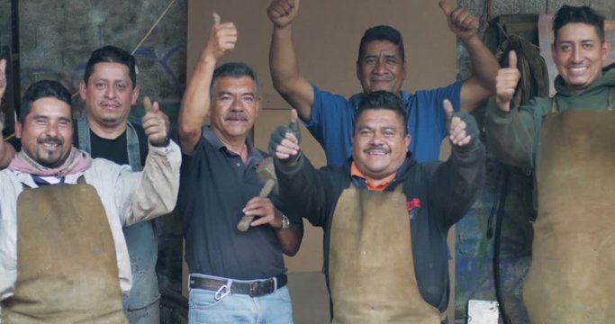Six smiling happy Mexican men give a thumbs up in their workshop