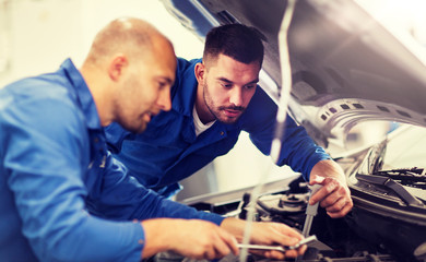 auto service, repair, maintenance and people concept - mechanic men with wrench repairing car at workshop