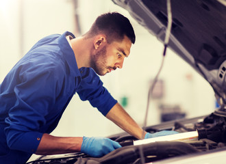 car service, repair, maintenance and people concept - auto mechanic man with lamp working at workshop