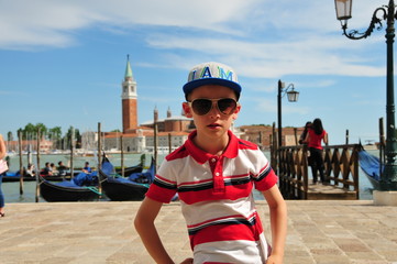 Obraz premium Boy in polo shirt with cap and sunglasses in front of the landmark of Venice