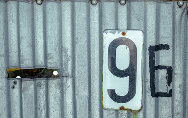 White Shabby Metal Plate With Black Nuber Nine and Six Nailed On Corrugated Old Iron Sheet