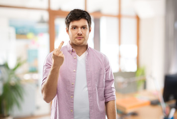 people concept - young man showing middle finger over office room background