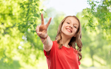 gesture and people concept - smiling teenage girl with long wavy hair in red t-shirt showing peace hand sign over green natural background