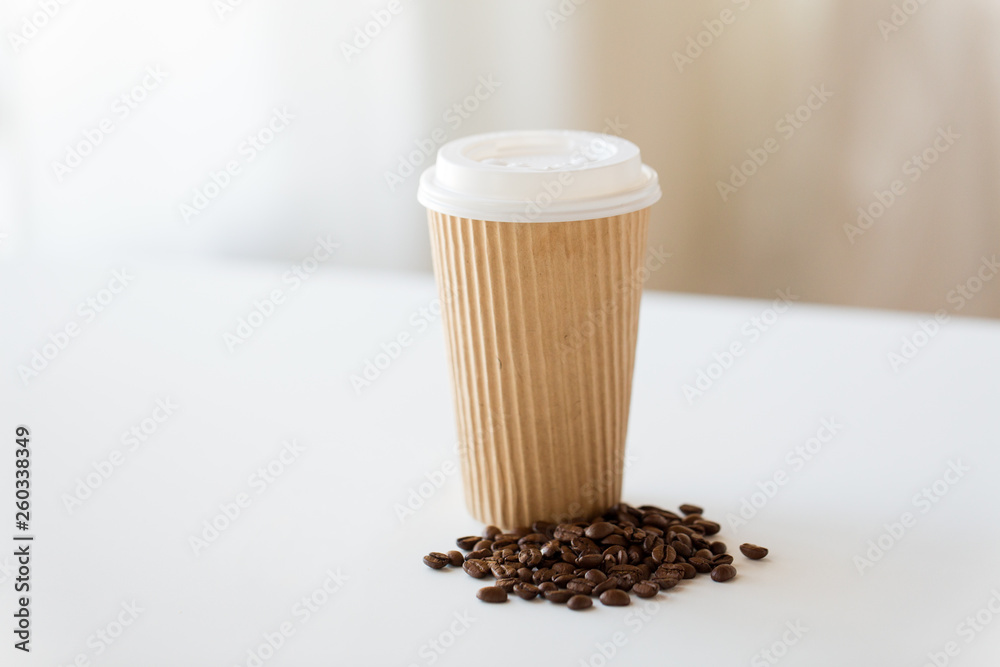 Poster caffeine and takeaway drinks concept - close up paper cup and roasted coffee beans on white table