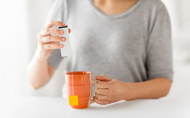 food additives and drinks concept - close up of woman adding sweetener to cup of tea