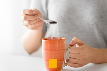 hot drinks concept - close up of woman adding sugar to cup of tea