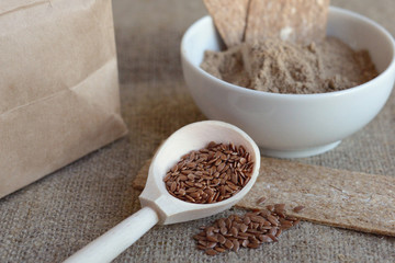 wooden spoon with flax seeds, next to flax flour, diet crispbread and craft pack