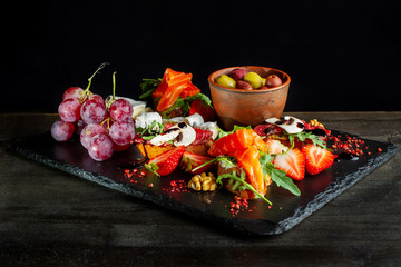 Fototapeta na wymiar Snacks laid out on black slate, cheese, grapes, sandwiches, strawberries, nuts.