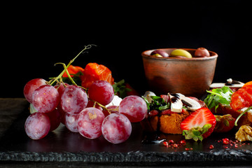 Snacks laid out on black slate, cheese, grapes, sandwiches, strawberries, nuts.