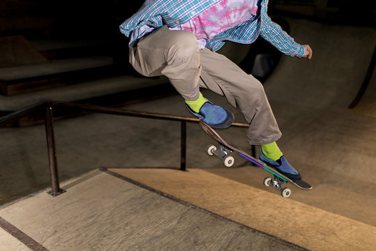 Action shot of unrecognizable young man doing skating stunt flipping skateboard at extreme park, shot with flash