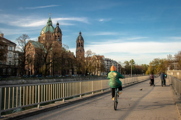 A kid rides a bycicle in the Isar river bridge with beautiful building scenery in Munich in a clear...
