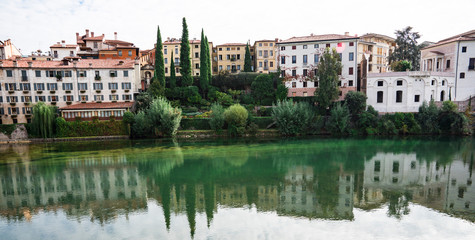 Fototapeta na wymiar colorful houses along river Brenta in Bassano del Grappa, Italy. With reflection in water