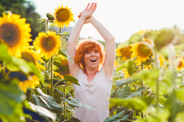 young girl enjoying nature on the field of sunflowers at sunset, portrait of the beautiful redheaded woman girl with a sunflowers in a sunny summer evening, hands raised up