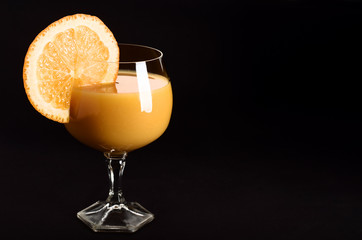 Orange juice in a glass with orange wedge on side on black background	