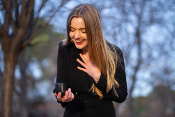 Beautiful young lady in stylish outfit looking at wedding ring in box while standing on blurred background of park