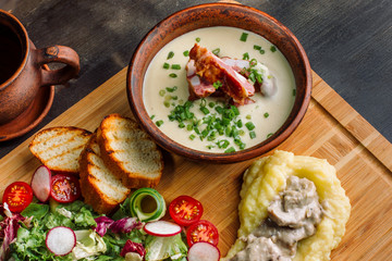 Pea soup with smoked meat in a clay plate, meat goulash with mushrooms and sauce.
