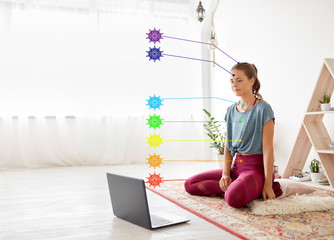 fitness, technology and healthy lifestyle concept - woman with laptop computer at yoga studio with seven chakra symbols