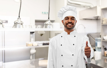 cooking, profession and people concept - happy male indian chef in toque showing thumbs up over restaurant kitchen background
