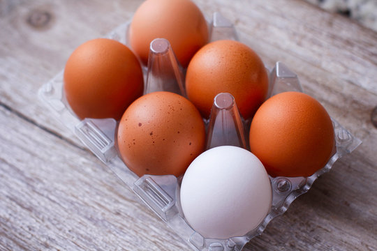 Set of different colours eggs in clear plastic box on wooden table. 