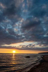 colorful sunset over calm sea beach with dark blue water and dramatic contrasty clouds