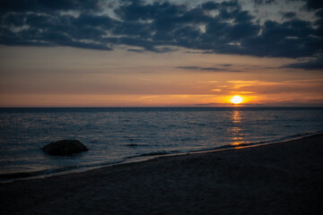 colorful sunset over calm sea beach with dark blue water and dramatic contrasty clouds