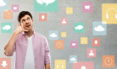technology, communication and people concept - young man showing phone call gesture over app icons on grey background