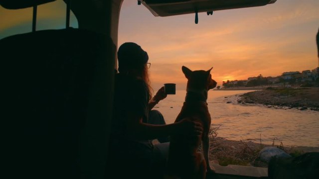 Slow motion romantic and dreamy shot from inside of camping van on young adventurous woman travel world with best friend puppy basenji dog, sips on tea or coffee calm and tranquil,camp vibes lifestyle