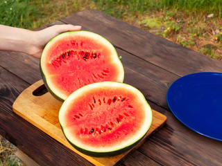 Female hands cut a ripe watermelon on a wooden table with a knife