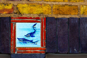 Blue fish tile set in a brick wall with red, yellow and black bricks