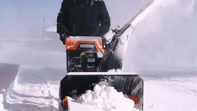 A man cleans the snow with a snowblower during a snowfall. Slow motion.