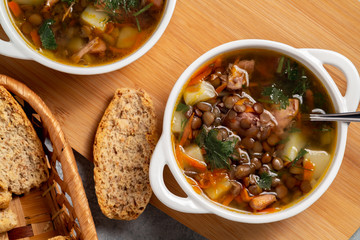 Two plates with lentil soup and chicken on a wooden board, top view