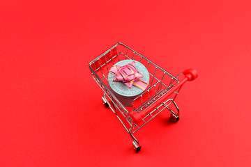 Blue present box with pink bow in a shopping cart on a red background.