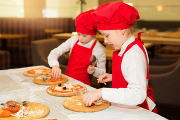 two beautiful cook girls in white shirts and red aprons in the restaurant make pizza