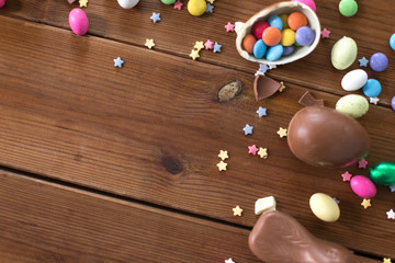 easter, sweets and confectionery concept - chocolate eggs, bunny and candy drops on wooden background