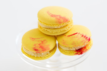 sweets, pastry and food concept - close up of lemon yellow macarons on glass confectionery stand over white background