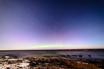 aurora borealis and stars in dark night over sea beach in winter