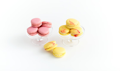 sweets, pastry and food concept - lemon yellow and pink macarons on glass confectionery stand over white background