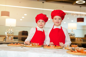 two beautiful cook girls in white shirts and red aprons in the restaurant make pizza