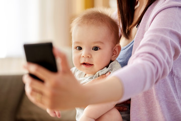 family and motherhood concept - close up of mother with little baby son taking selfie by smartphone at home
