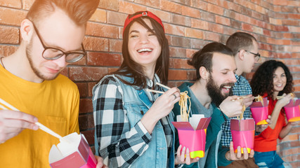 Millennials nutrition. Young coworkers having fun during lunch break, eating noodles with chopsticks. Fast food meal.