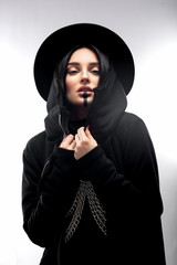 Beautiful woman in black clothes and hat over isolated gray background